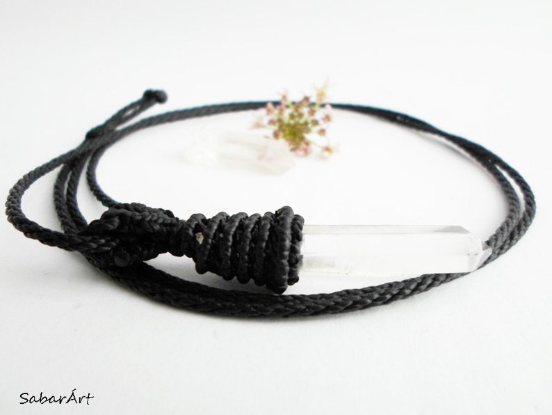 May include: A clear quartz crystal pendant on a black cord necklace. The cord is tied with a knot at the top of the pendant.