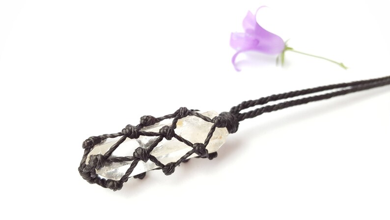 May include: A clear quartz crystal pendant wrapped in a black macrame cord necklace.