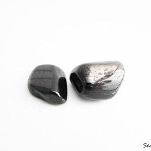 May include: Two black tumbled stones, one is slightly larger than the other. The stones have a smooth, polished surface.