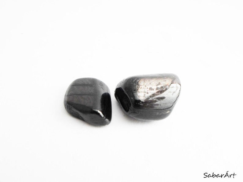 May include: Two black tumbled stones, one is slightly larger than the other. The stones have a smooth, polished surface.
