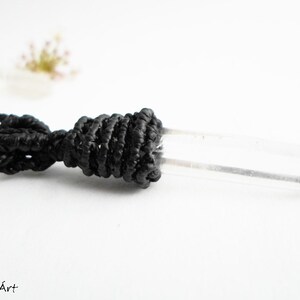 May include: A clear quartz crystal pendant on a black cord necklace. The crystal is long and slender, with a smooth, polished surface. The cord is knotted at the top of the crystal, creating a secure and stylish look.
