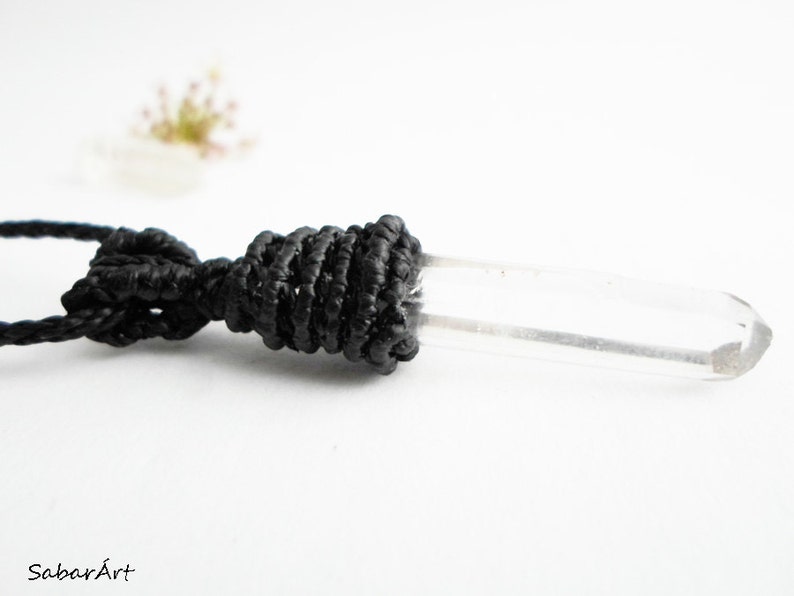 May include: A clear quartz crystal pendant on a black cord necklace. The crystal is long and slender, with a smooth, polished surface. The cord is knotted at the top of the crystal, creating a secure and stylish look.