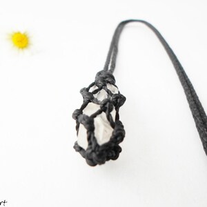 May include: A white crystal is encased in a black macrame net, hanging from a black cord. The crystal is a natural, irregular shape.