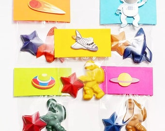 May include: Six small bags filled with colorful space-themed party favors. Each bag includes a star-shaped crayon, a rocket, astronaut, or UFO cutout, and a small card with a space-themed image.