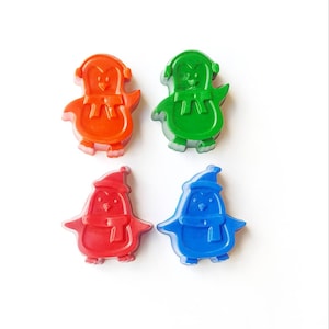 May include: Four penguin-shaped crayons in red, blue, green, and orange. Each crayon has a white hat and scarf.