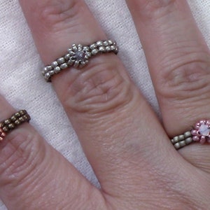 Puede incluir: Tres anillos de cuentas con dijes en forma de flor. Los anillos están hechos con cuentas de diferentes colores y presentan un dije de flor azul, rosa y blanco.