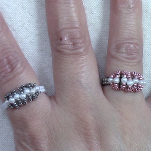 May include: Two beaded rings on a hand. One ring is silver with white beads and the other is rose gold with white beads.