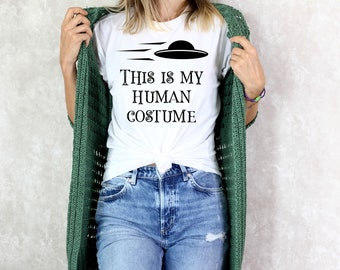 May include: White t-shirt with a black graphic of a flying saucer and the text "This is my human costume".