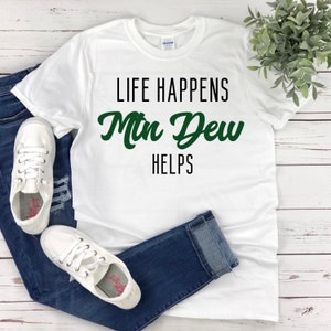 May include: White t-shirt with black text that reads "Life Happens Mtn Dew Helps" in green.