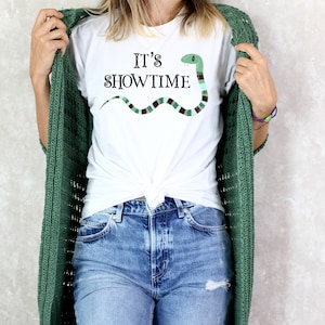 May include: White t-shirt with a green snake graphic and the text "It's Showtime".