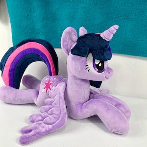 May include: Purple plush toy of Twilight Sparkle from My Little Pony. She has a pink and purple rainbow mane, a dark blue mane, a purple horn, and a white star on her flank.