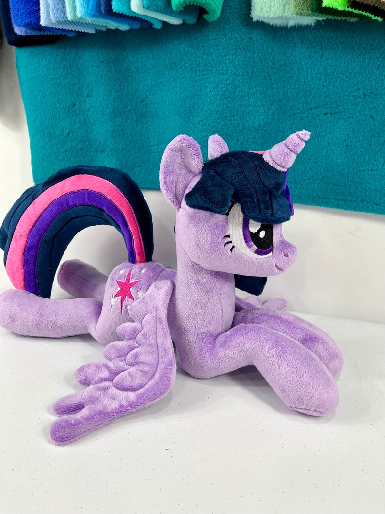 May include: Purple plush toy of Twilight Sparkle from My Little Pony. She has a pink and purple rainbow mane, a dark blue mane, a purple horn, and a white star on her flank.
