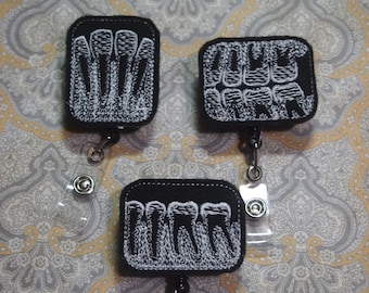 May include: Three black fabric badge holders with white embroidered images of teeth. Each holder has a clear plastic retractable badge reel.