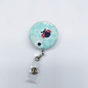 May include: A light blue retractable badge holder with a white and red ladybug on a floral pattern.