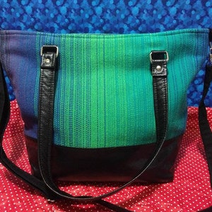 May include: A blue and green striped tote bag with black leather straps and a black leather bottom.