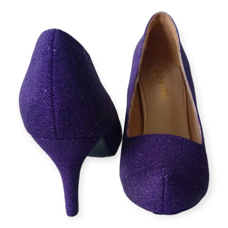 Puede incluir: Un par de zapatos de tac&oacute;n alto de purpurina morada. Los zapatos tienen punta puntiaguda y tac&oacute;n de aguja.