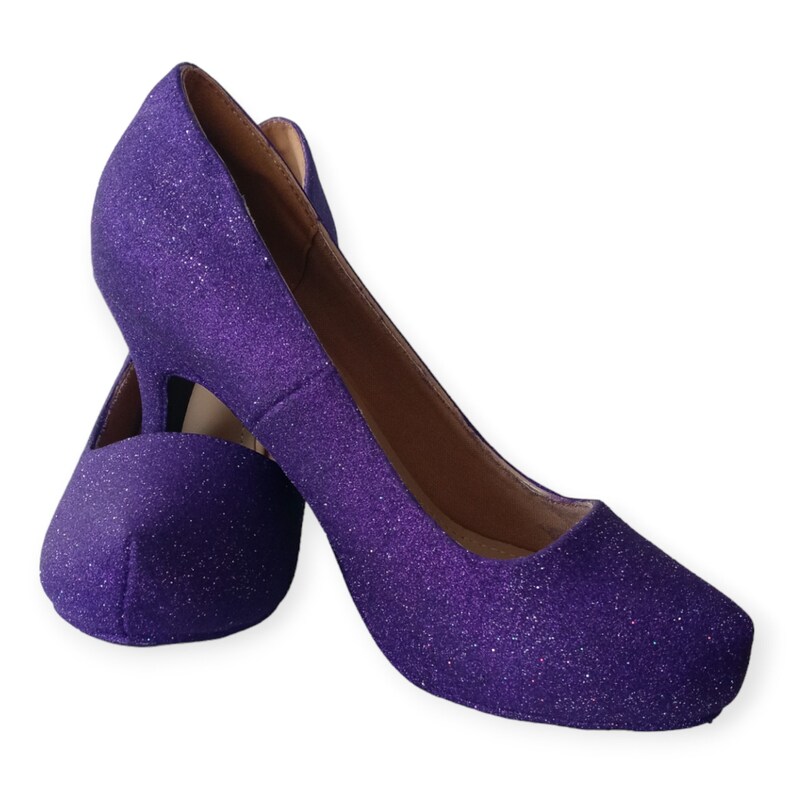 Puede incluir: Un par de zapatos de tac&oacute;n alto de purpurina morada. Los zapatos tienen la punta cerrada y una forma redondeada.