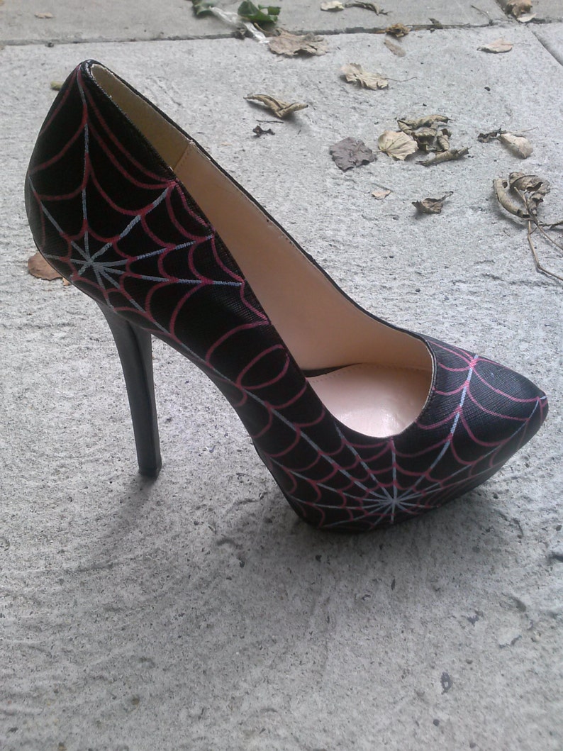 May include: Black high-heeled pump with a spiderweb design in white and pink.