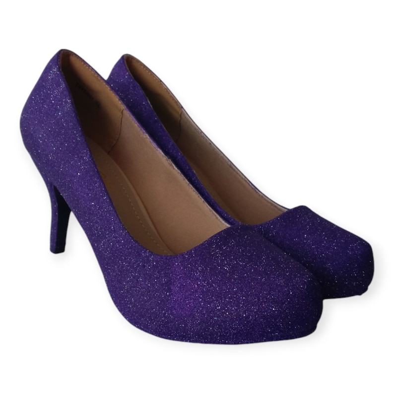 Puede incluir: Un par de zapatos de tac&oacute;n alto de purpurina morada. Los zapatos tienen una punta puntiaguda y un cierre trasero.