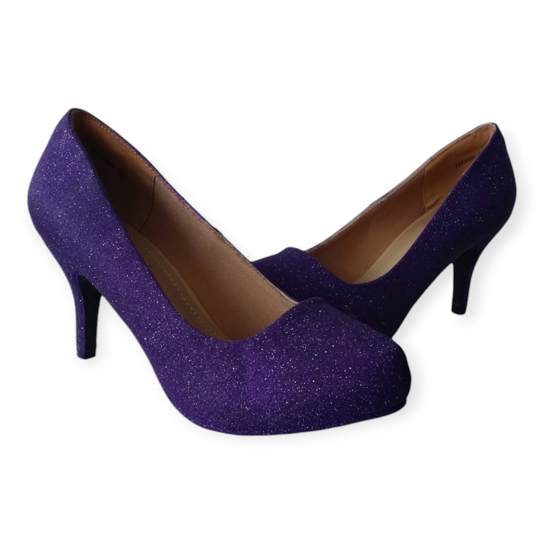 Puede incluir: Un par de zapatos de tac&oacute;n alto de purpurina morada. Los zapatos tienen una punta puntiaguda y un tac&oacute;n fino.