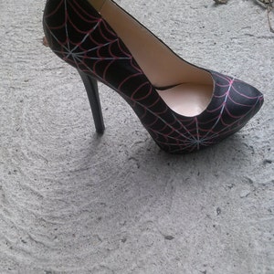 May include: Black high-heeled shoe with a spiderweb design in red and white.