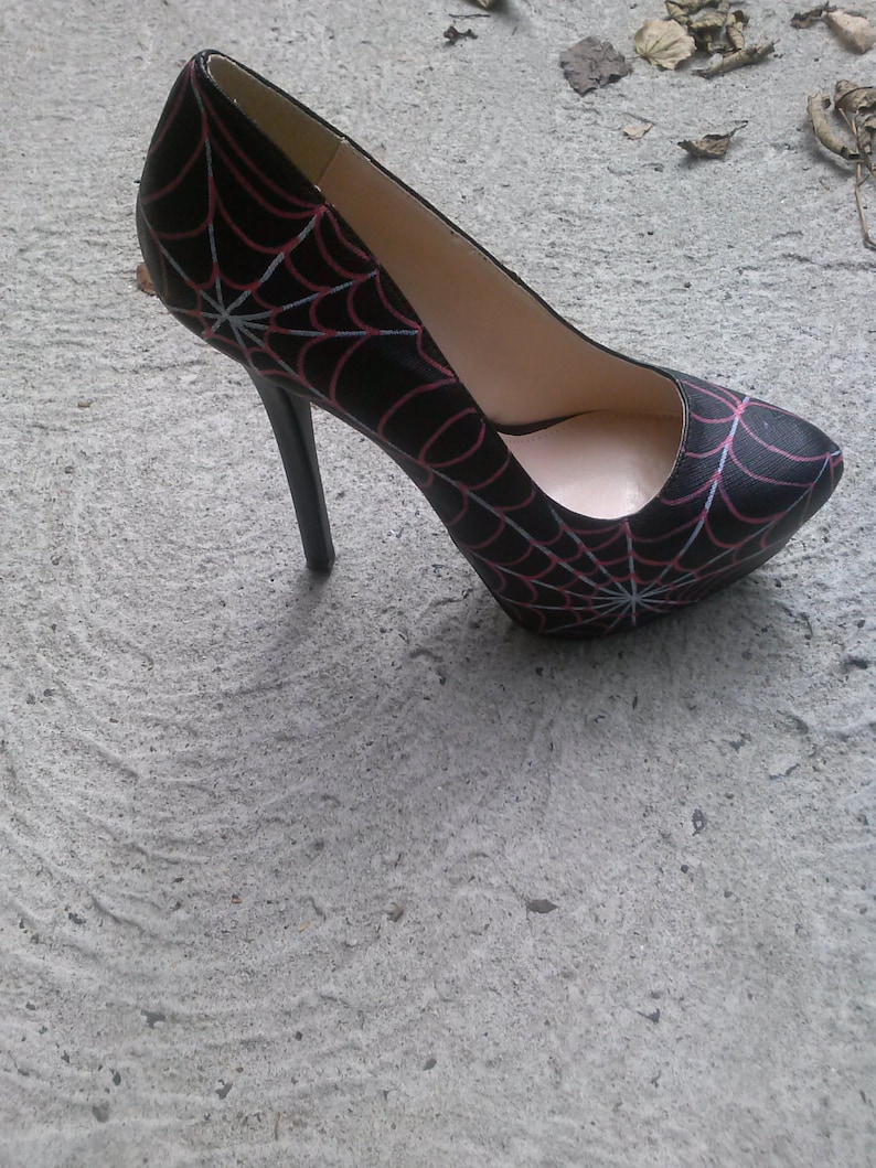 May include: Black high-heeled shoe with a spiderweb design in red and white.