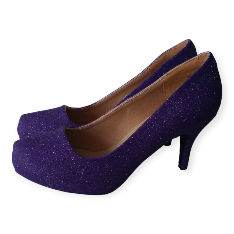 Puede incluir: Un par de zapatos de tac&oacute;n alto de purpurina morada. Los zapatos tienen una punta puntiaguda y un tac&oacute;n fino.