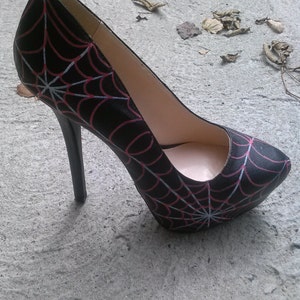May include: Black high-heeled pump with a spiderweb design in red and white.