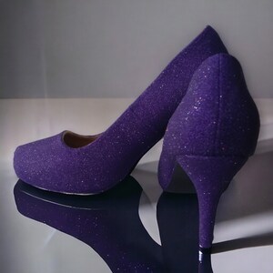 Puede incluir: Un par de tacones altos de purpurina morada con punta puntiaguda y tac&oacute;n de aguja.
