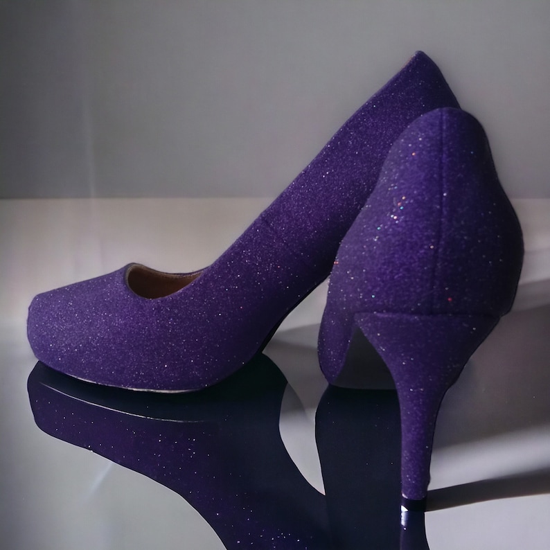 Puede incluir: Un par de tacones altos de purpurina morada con punta puntiaguda y tac&oacute;n de aguja.