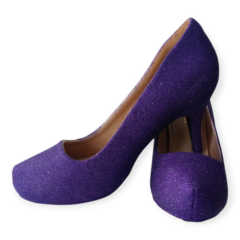 Puede incluir: Un par de tacones altos de purpurina morada. Los tacones son de punta y tienen un tac&oacute;n fino de aguja.