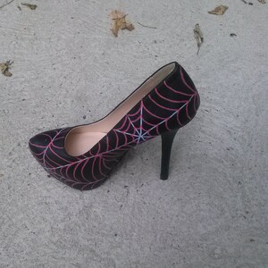 May include: Black high-heeled pump with a pink spiderweb design.