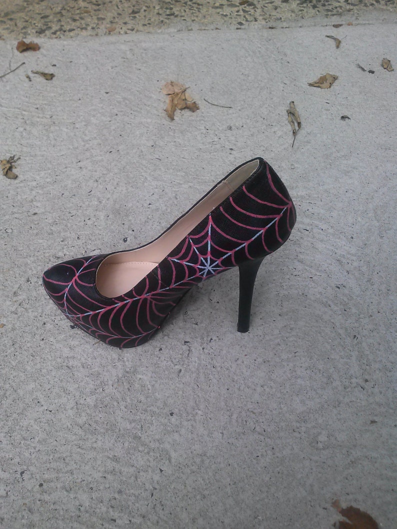 May include: Black high-heeled pump with a pink spiderweb design.