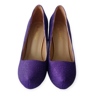 Puede incluir: Un par de zapatos de tac&oacute;n de purpurina morada. Los zapatos tienen punta puntiaguda y tac&oacute;n bajo. El nombre de la marca "Dream Pairs" est&aacute; impreso en el interior de cada zapato.