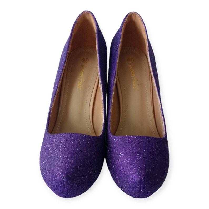 Puede incluir: Un par de zapatos de tac&oacute;n de purpurina morada. Los zapatos tienen punta puntiaguda y tac&oacute;n bajo. El nombre de la marca "Dream Pairs" est&aacute; impreso en el interior de cada zapato.