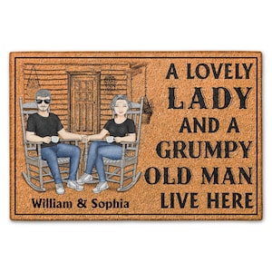 以下が含まれることがあります： 茶色の背景と黒い縁取りの長方形のドアマット。マットには、マグカップを持ったロッキングチェアに座っているカップルのイラストが描かれています。「A LOVELY LADY AND A GRUMPY OLD MAN LIVE HERE」というテキストと、下に「William & Sophia」という名前があります。