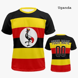 May include: A short-sleeved t-shirt with the Ugandan flag design. The shirt has horizontal stripes of black, yellow, and red. A white circle on the front displays a gray and red crested crane. The back of the shirt has the text "YOUR NAME" and the number "00".