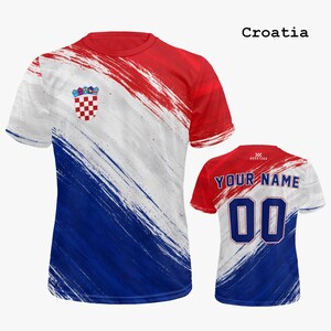 Op de afbeelding: Een rood, wit en blauw Kroati&euml; voetbalshirt met een penseelstreken ontwerp. De voorkant heeft het Kroatische wapen. De achterkant toont de tekst "YOUR NAME" boven het nummer "00". Het woord "Croatia" staat bovenaan gedrukt.