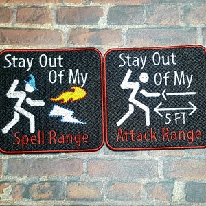 May include: Two black and red embroidered patches with white text. The left patch says "Stay Out Of My Spell Range" and features a stick figure with a wizard hat casting a spell. The right patch says "Stay Out Of My Attack Range" and features a stick figure with a sword and a 5 ft range indicator.