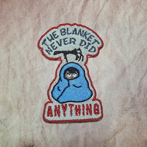 May include: Embroidered patch with a cartoon character wrapped in a blue blanket. The text above the character reads "The Blanket Never Did" and the text below the character reads "Anything".
