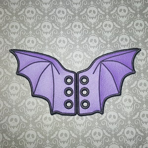 Peut inclure: Ailes de chauve-souris violettes avec un laçage de style corset noir. Les ailes sont en tissu doux et pelucheux et ont une surface légèrement texturée.