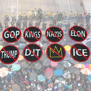 Puede incluir: Vista aérea de una multitud con paraguas y una fila de policías. Se ven ocho parches negros con texto blanco, cada uno tachado con una línea roja. El texto incluye "GOP", "KINGS", "NAZIS", "ELON", "TRUMP", "DJT", una corona e "ICE".