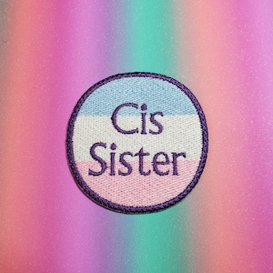 May include: A round, purple-trimmed patch with a light blue, white, and pink stripe design. The text "Cis Sister" is embroidered in purple on the patch.
