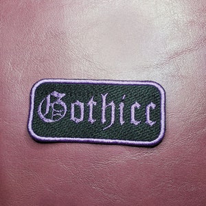 May include: Purple embroidered patch with the word "Gothjicc" in a gothic font on a black background.