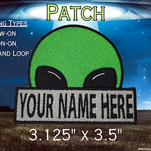 Puede incluir: Un parche bordado con una cabeza de alienígena verde con ojos negros sobre una banda rectangular gris con el texto negro YOUR NAME HERE. El parche mide 3,125 pulgadas por 3,5 pulgadas y ofrece opciones de fijación para coser, planchar o con velcro.