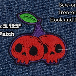 May include: A 3" x 3.125" embroidered patch featuring two red cherries with skull faces. The cherries have purple stems and green leaves. The patch is available in sew-on, iron-on, and hook and loop options.