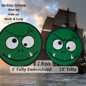 May include: Two embroidered green goblin face patches. The larger patch is 3 inches in diameter and the smaller patch is 2.5 inches in diameter. Both patches have a white stitched smile and eyes.
