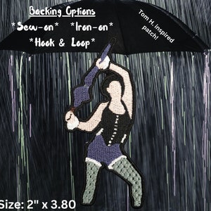 May include: An embroidered patch featuring a figure holding an umbrella, with text reading Backing Options, Sew-on, Iron-on, Hook & Loop, Tom H. inspired patch, and Umbrella ella AYE AYE. The patch measures 2 inches by 3.80 inches in size.