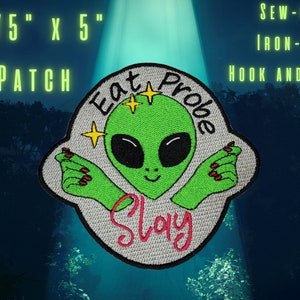 May include: A green alien with red fingernails and a white background. The alien is wearing a white hat with the words "Eat Probe Slay" in pink. The patch is 4.75 inches by 5 inches and can be sewn on, ironed on, or attached with hook and loop.
