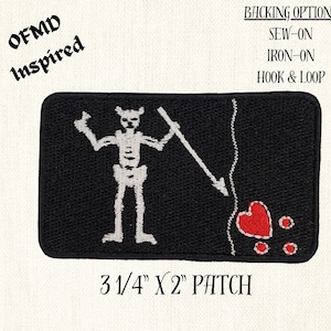 Puede incluir: Un parche bordado en blanco y negro con un esqueleto sosteniendo una lanza con un corazón rojo y tres puntos rojos. El parche mide 8,3 cm por 5,1 cm y tiene el texto "OFMD Inspired" y "OPCIONES DE SOPORTE: COSER, PLANCHAR, GANCHO & BUCLE" impreso en el fondo blanco.